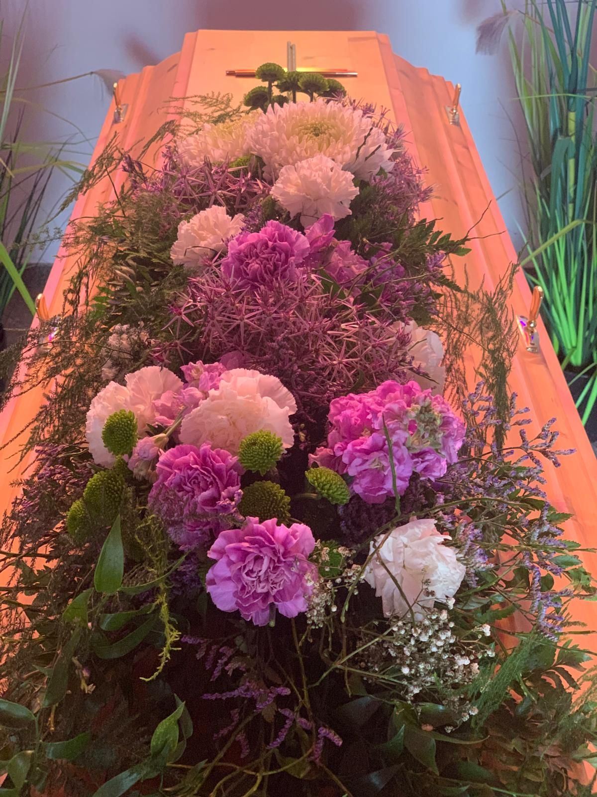 Trauersarg mit Blumenarrangement, darunter violette, rosa und weiße Blumen.