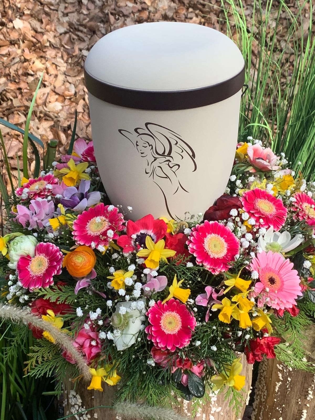 Urne mit Engelszeichnung, umgeben von bunten Blumen.