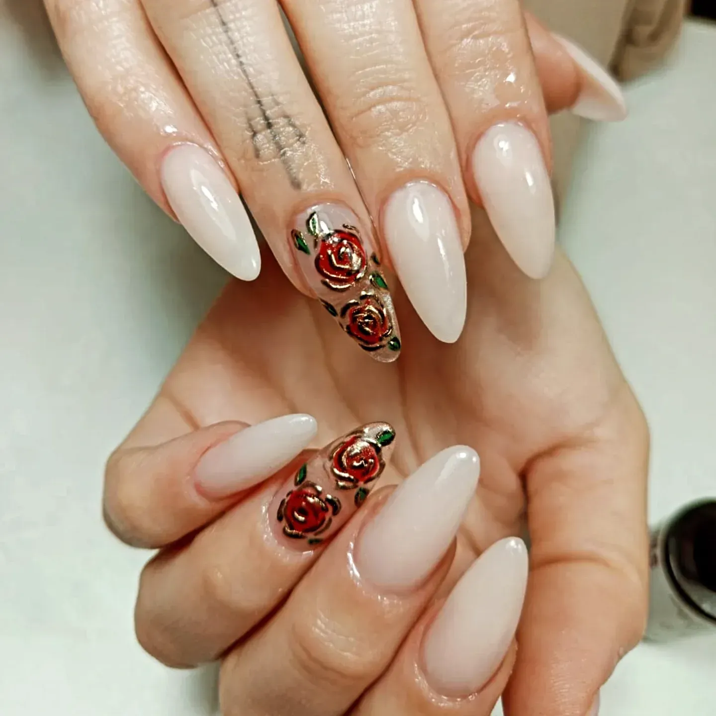 Primer plano de manos con uñas color nude almendradas y uñas decoradas con flores color oro rosa.