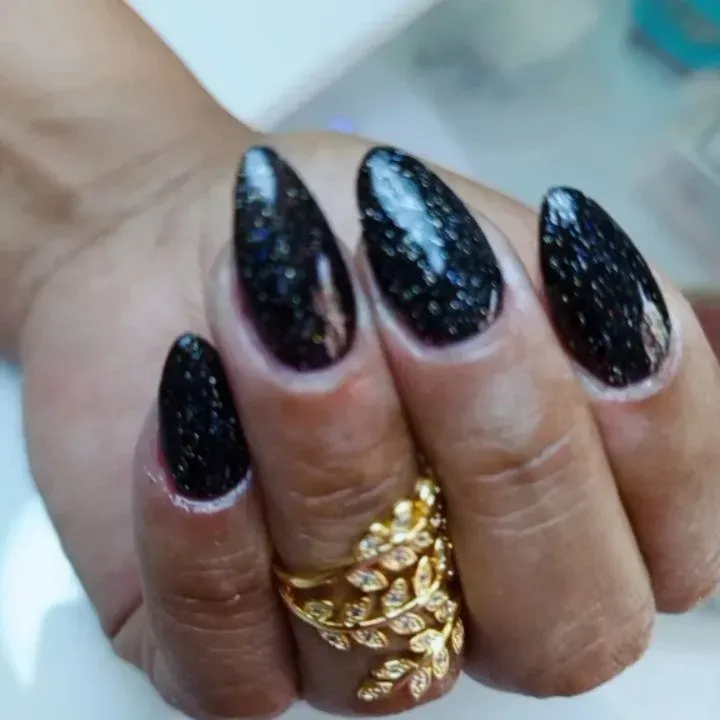 Mano con uñas largas negras con purpurina y anillos dorados, primer plano.