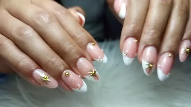 Primer plano de manos con manicura francesa en rosa y blanco y decoración dorada en las uñas.