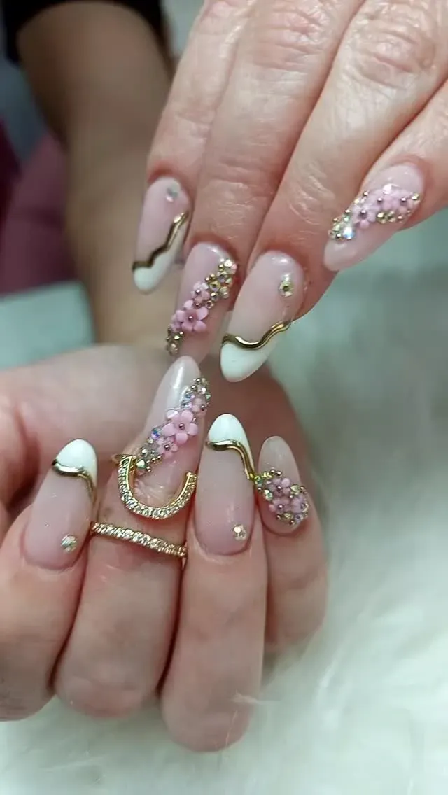 Manos con uñas largas almendradas, purpurina rosa y puntas francesas blancas, sosteniendo una pulsera de cadena dorada.