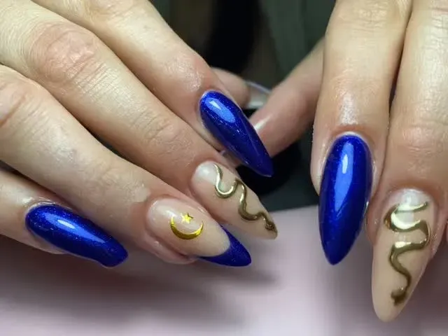 Manos con uñas largas de color azul cobalto y beige decoradas con espirales doradas.