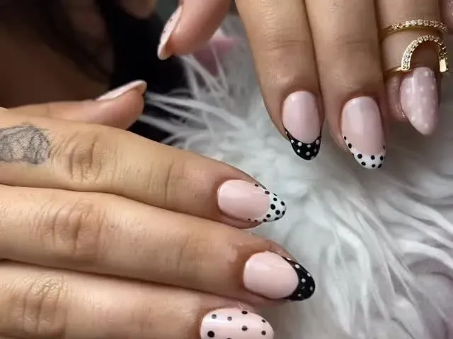 Manos con uñas rosas y puntas pintadas con lunares negros, descansando sobre una superficie blanca y esponjosa.