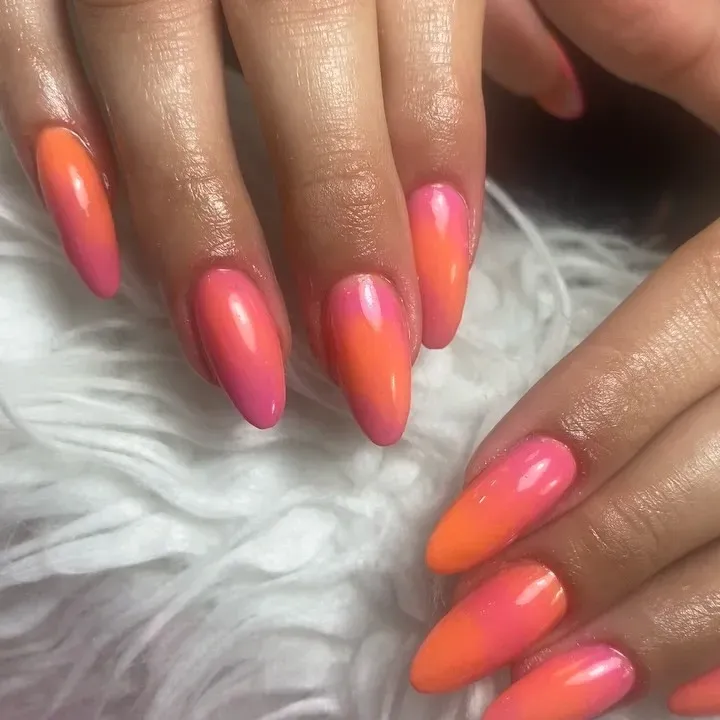 manicura degradada en tonos rosa y naranja, descansando sobre una superficie blanca y esponjosa.