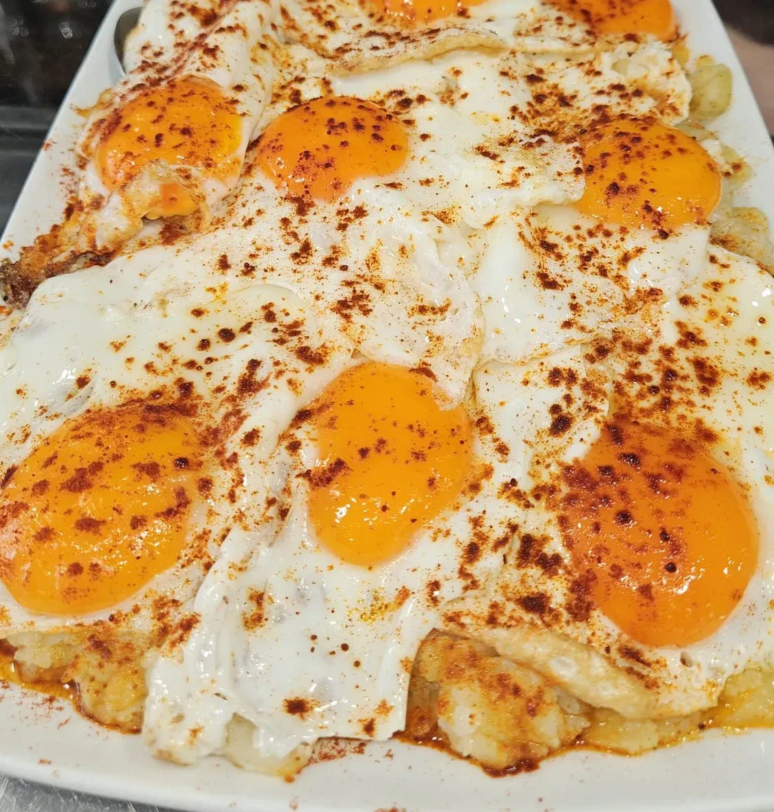 Un plato blanco cubierto con huevos fritos y patatas.
