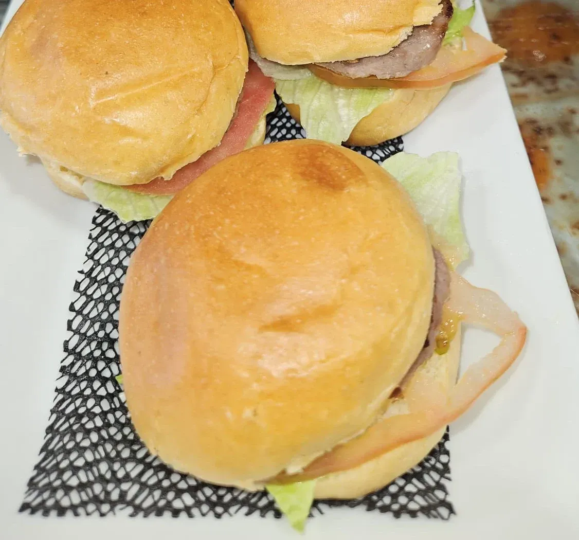 Tres hamburguesas en un plato blanco con lechuga y tomates.