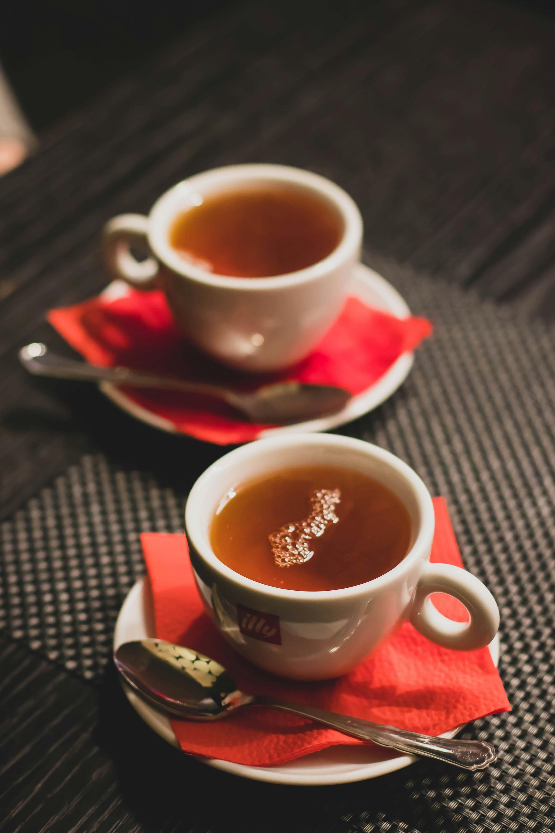 Dos tazas de té en platillos con cucharas sobre una mesa.