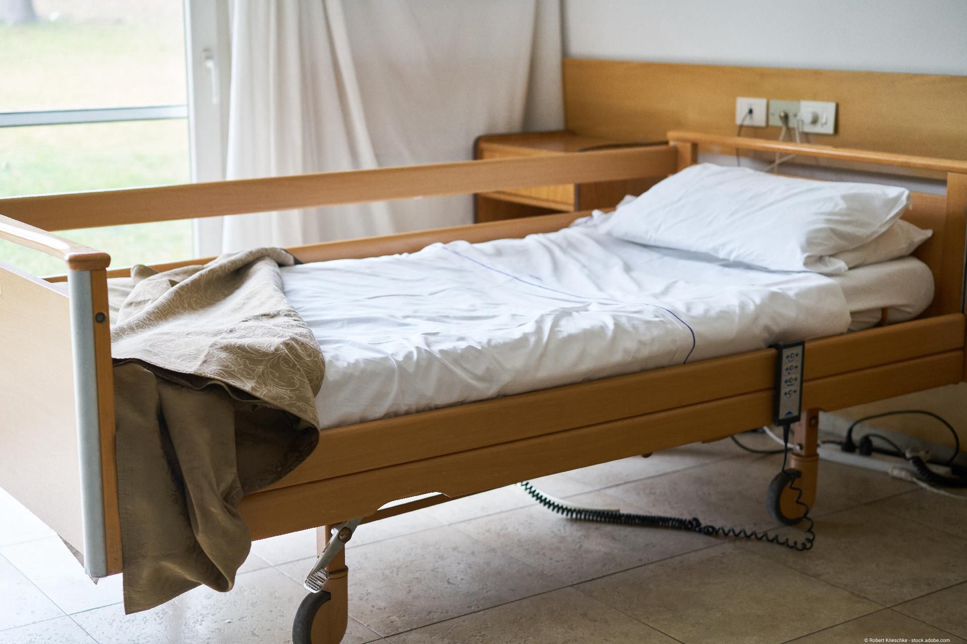 Pflegebett in hellem Zimmer mit Bettgitter und Rollen, geeignet für häusliche Pflege.