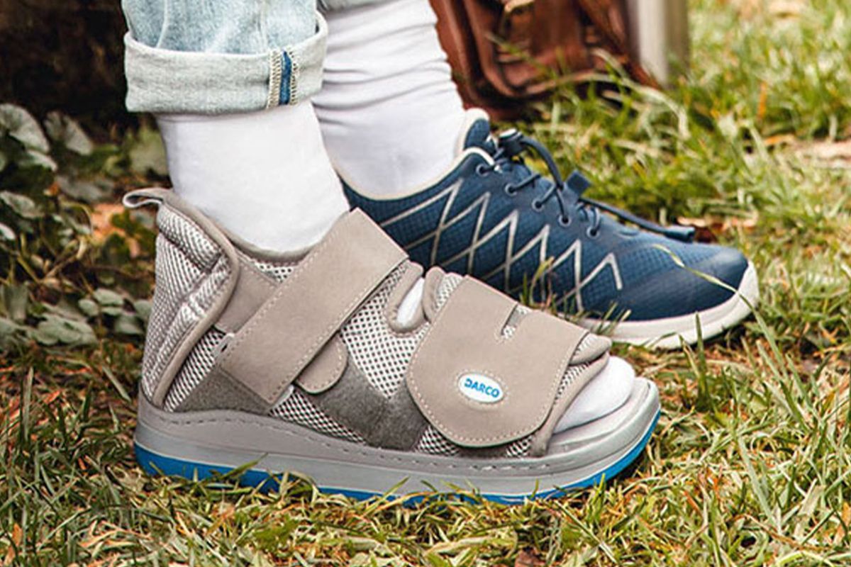 Orthopädische Stiefel und ein spezieller Therapieschuh stehen auf Gras im Freien, geeignet für Stabilisierung und Reha.