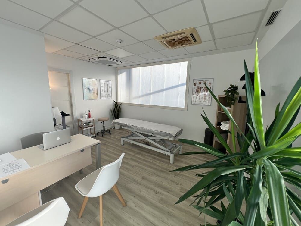 Un consultorio médico con un escritorio, sillas y una cama.