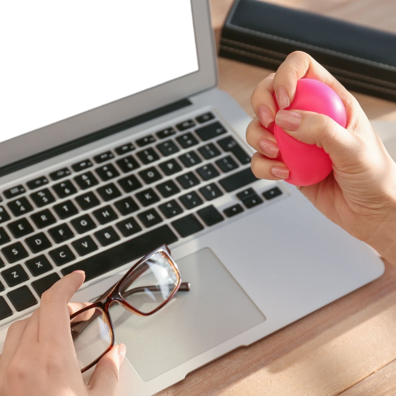 Una persona sosteniendo una pelota rosa frente a una computadora portátil.
