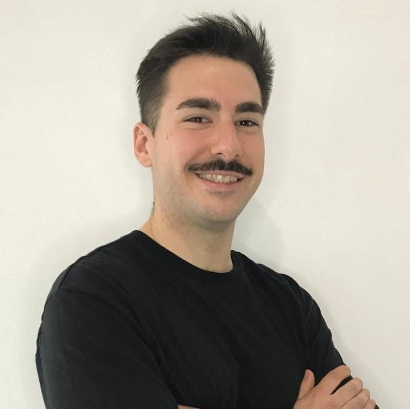 Un hombre con bigote sonríe con los brazos cruzados.