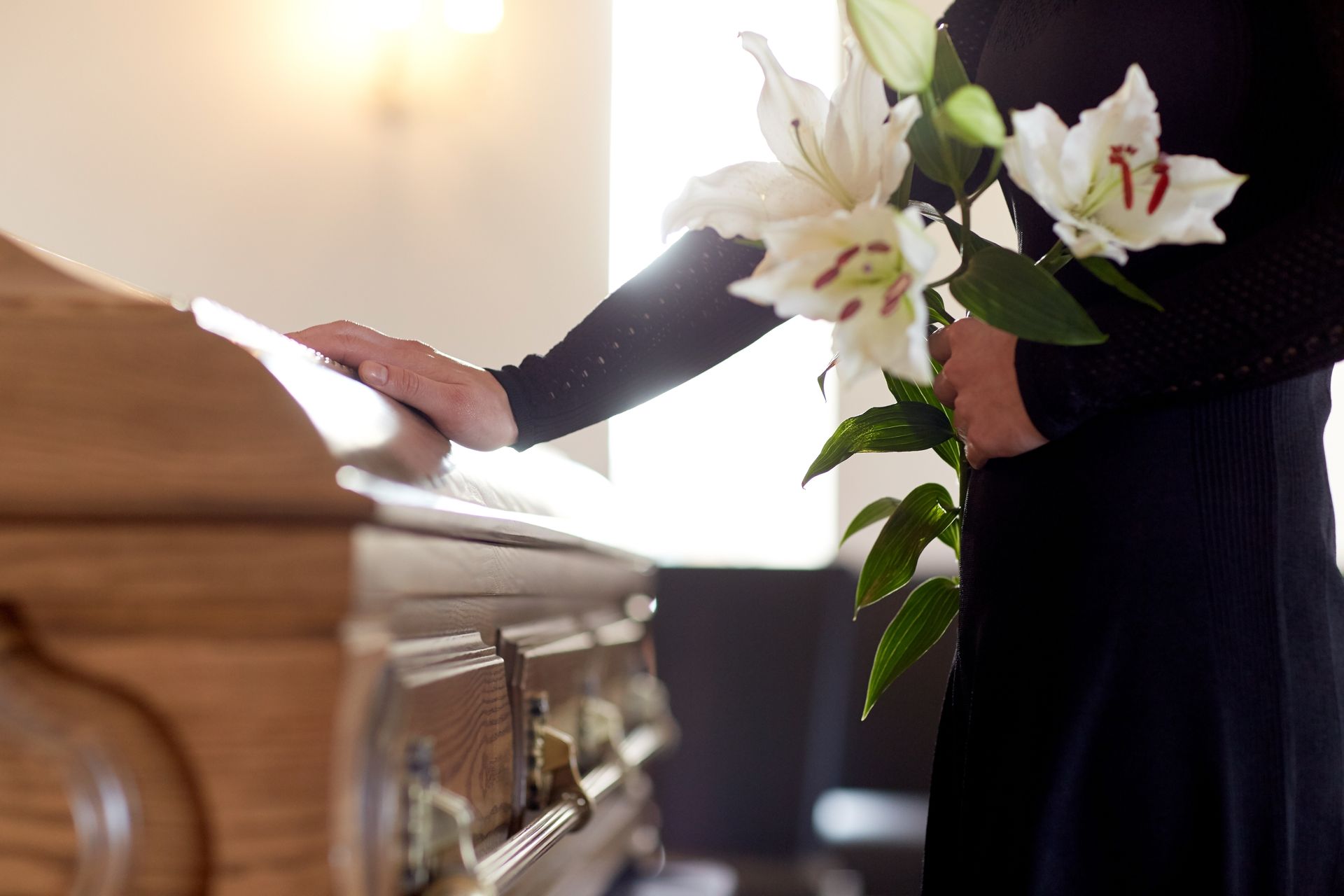 Une main se pose sur un cercueil avec des lys à la main