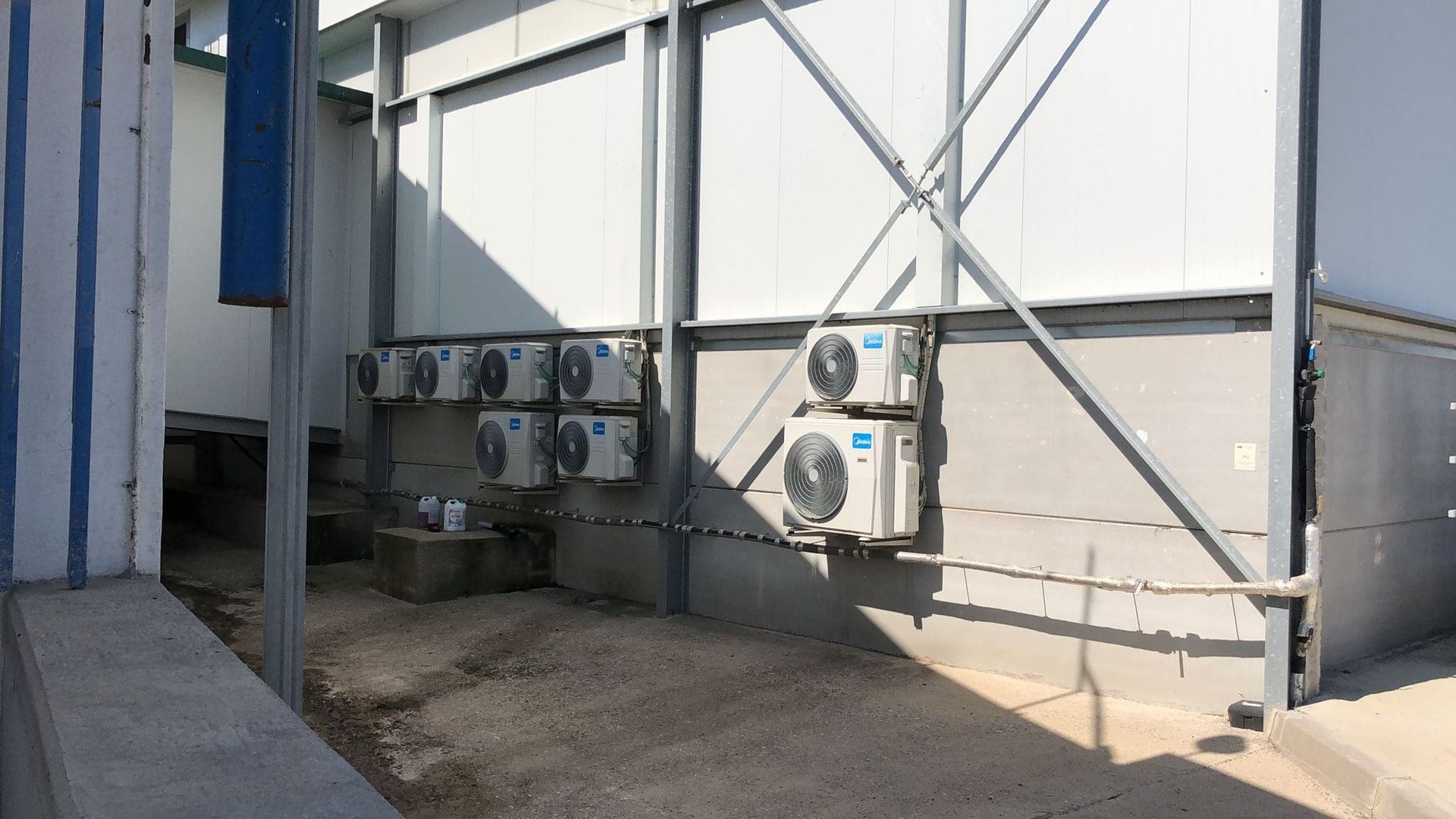 Varias unidades de aire acondicionado instaladas en la pared exterior de un edificio industrial blanco.