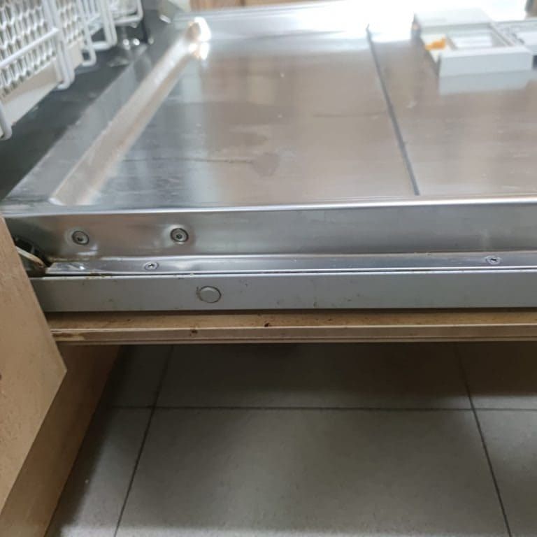 Una puerta abierta del lavavajillas que deja ver el interior de acero inoxidable y el borde de la rejilla inferior.