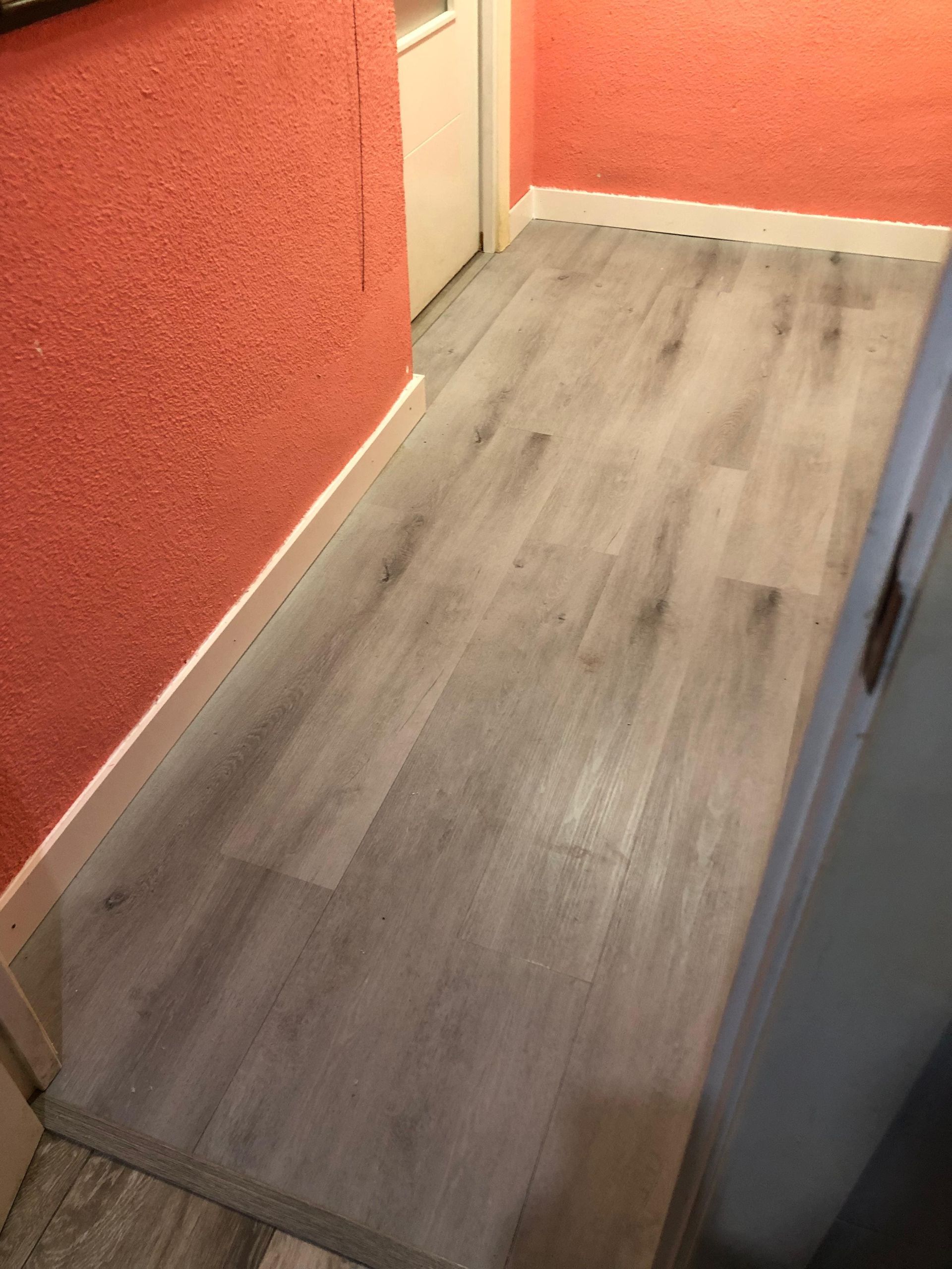 Un pasillo con suelo de tablones de imitación madera gris y paredes texturizadas de color naranja, visto desde una puerta.