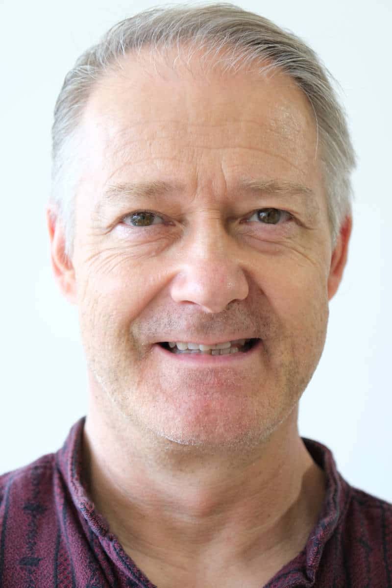 Ein Mann in einem lila Hemd lächelt in die Kamera.