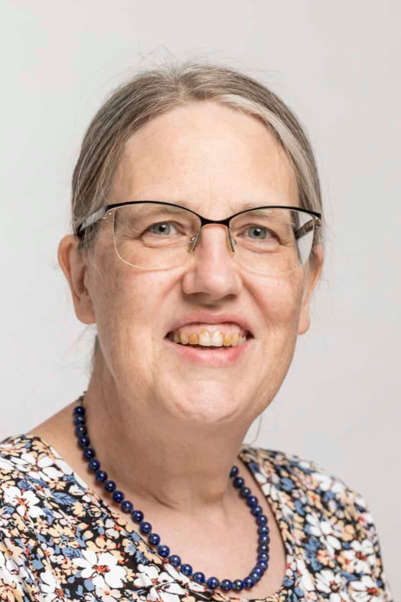 Eine Frau mit Brille und Halskette lächelt in die Kamera.