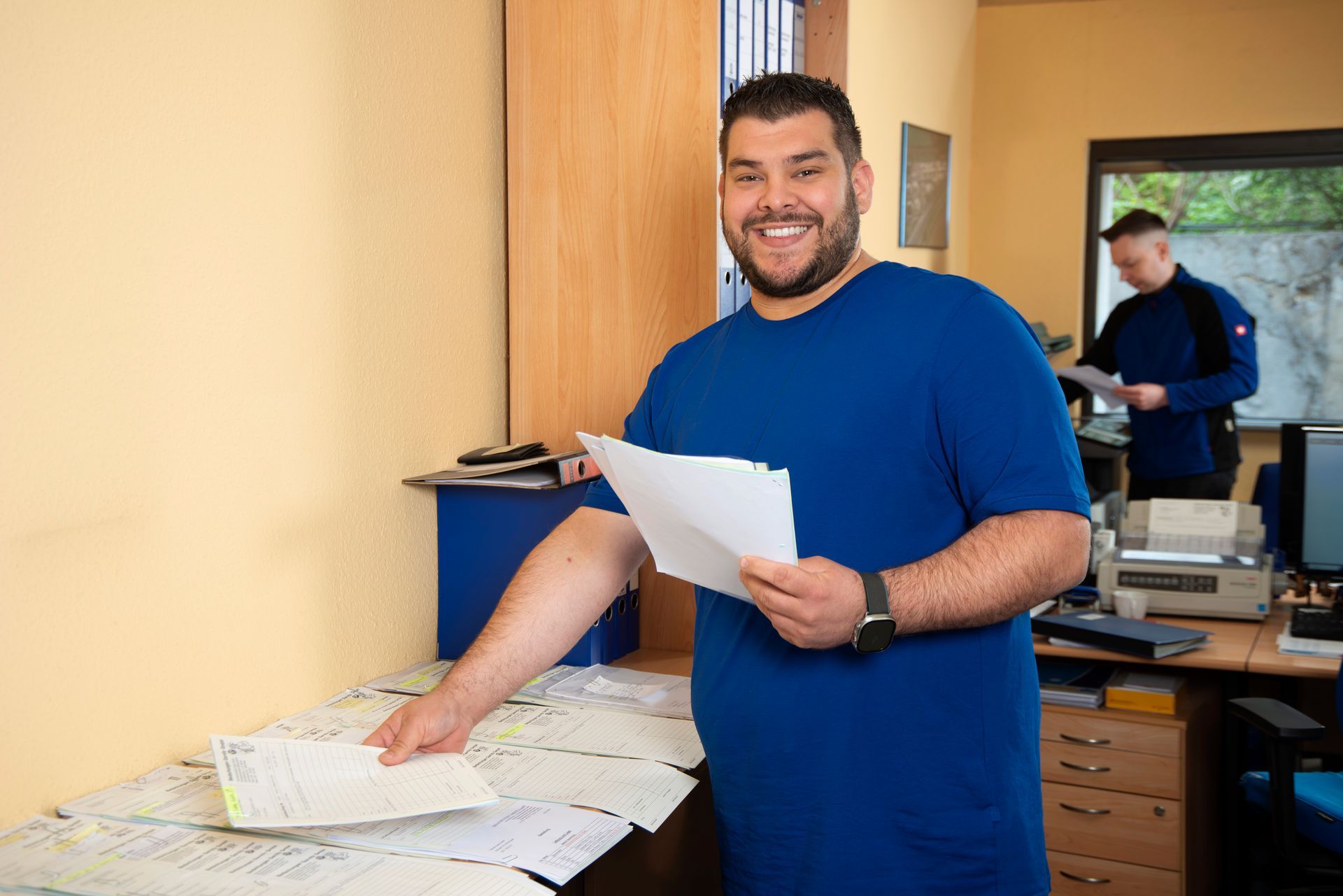 Ein Mann in einem blauen Hemd hält in einem Büro ein Stück Papier.