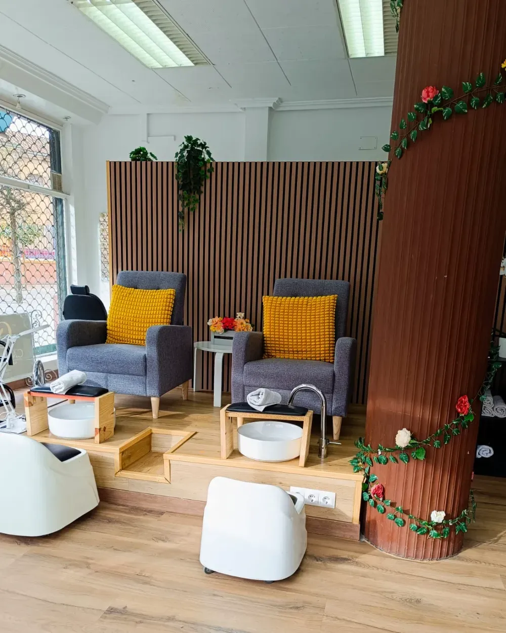 Dos sillas grises con almohadas amarillas y cuencos de pedicura blancos sobre una plataforma de madera, dentro de un salón