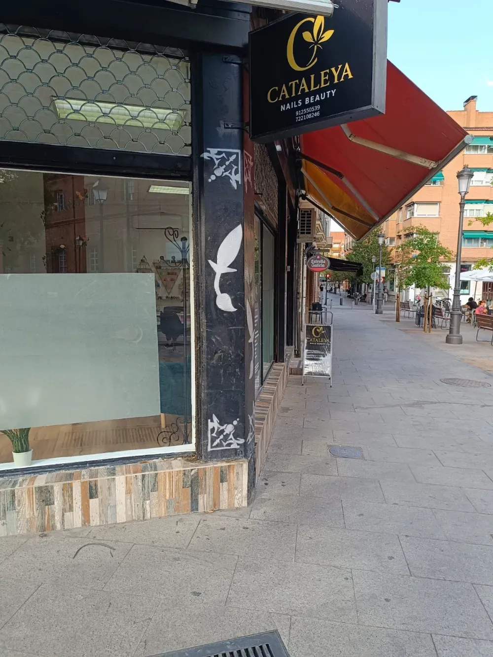 El escaparate de la esquina de Cataleya Hair & Beauty en una calle peatonal soleada, con un cartel negro y toldos rojos.