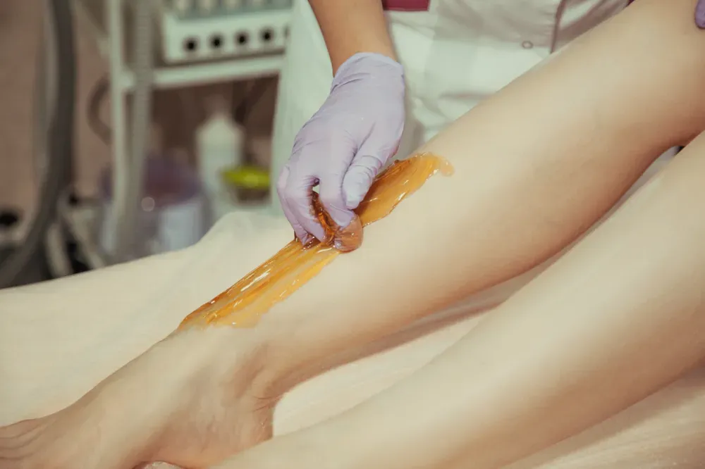 Una mano enguantada aplica cera depilatoria de color ámbar en la parte inferior de la pierna durante un tratamiento 