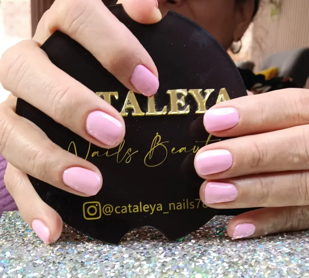 Unas manos con uñas cuidadas de color rosa claro sostienen un cartel comercial circular negro con un texto dorado