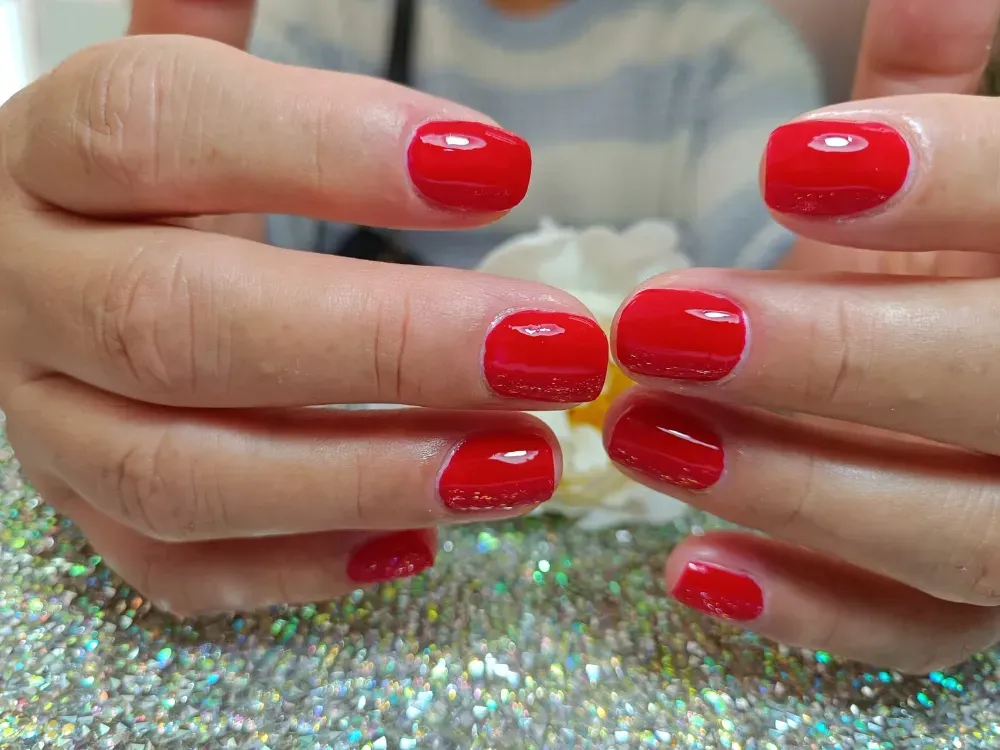 Primer plano de unas manos con uñas perfectamente cuidadas, de un rojo vibrante, unidas sobre una superficie brillante