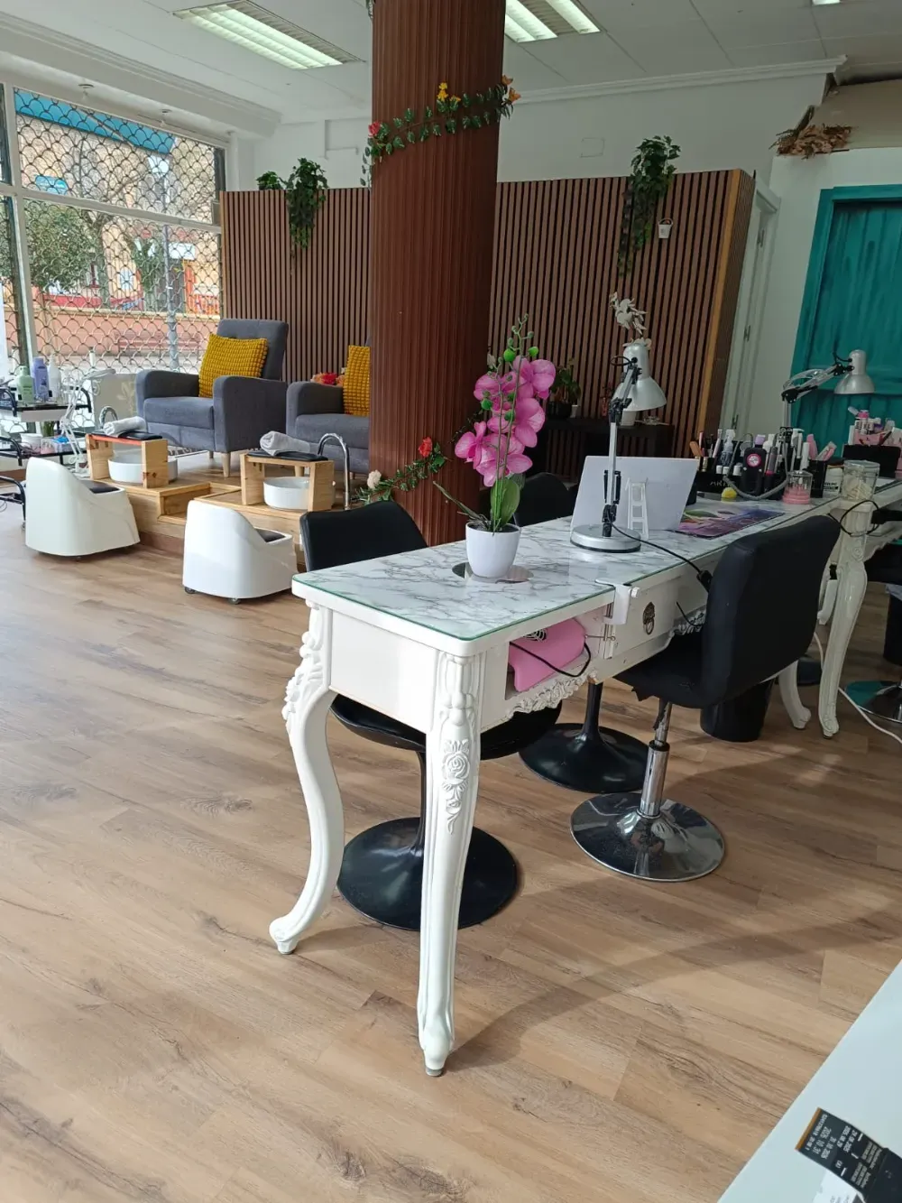 El interior de un salón de uñas cuenta con una mesa de manicura blanca adornada, sillas de pedicura, una gran columna 