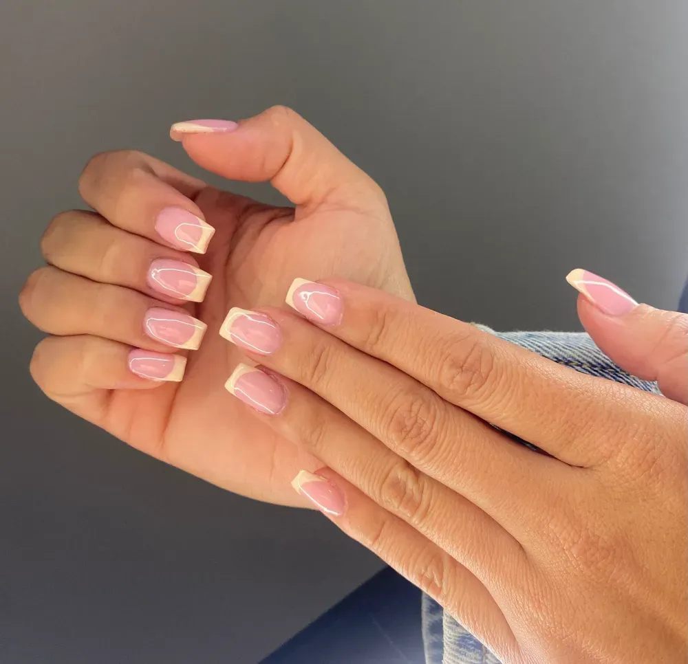 Manos que muestran una manicura con uñas de color rosa claro y puntas francesas de color amarillo pálido sobre 
