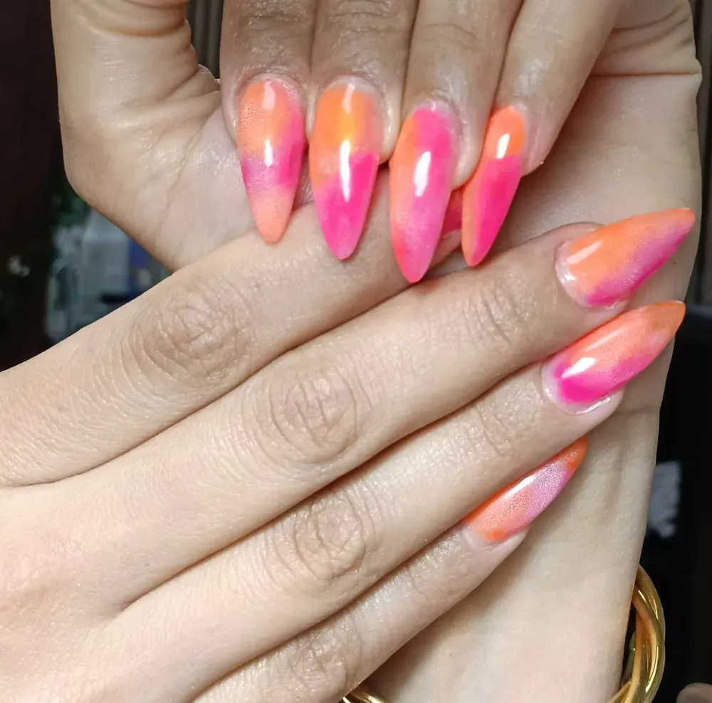 Primer plano de uñas en forma de almendra con un diseño degradado ombré en rosa y naranja vibrante.