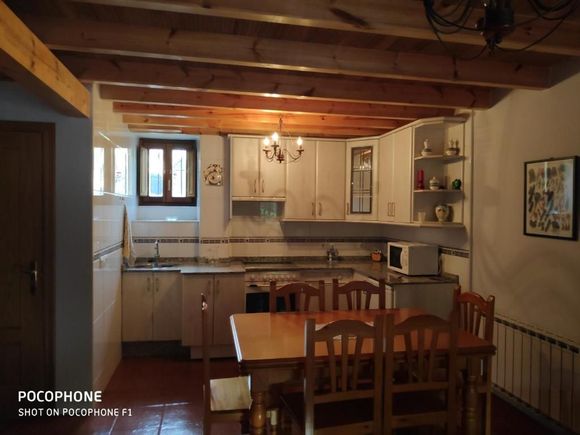 Cocina con vigas de madera, armarios blancos y mesa de comedor con sillas.