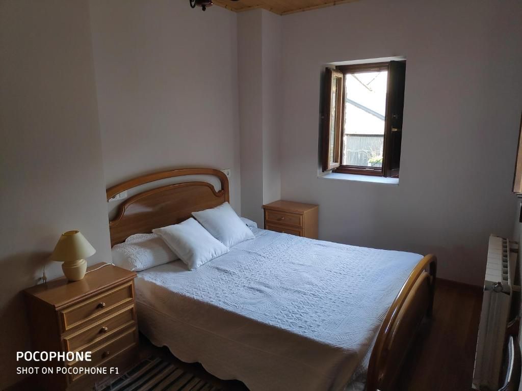 Dormitorio con cama, mesitas de noche, ventana y radiador.