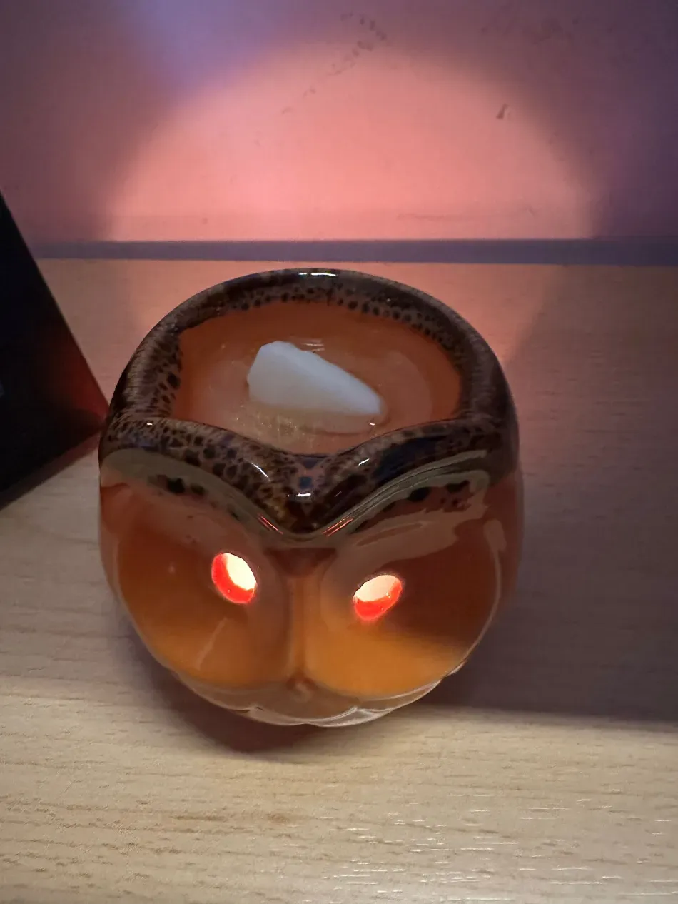 Un portavelas naranja con forma de búho que brilla con luces rojas sobre una mesa.