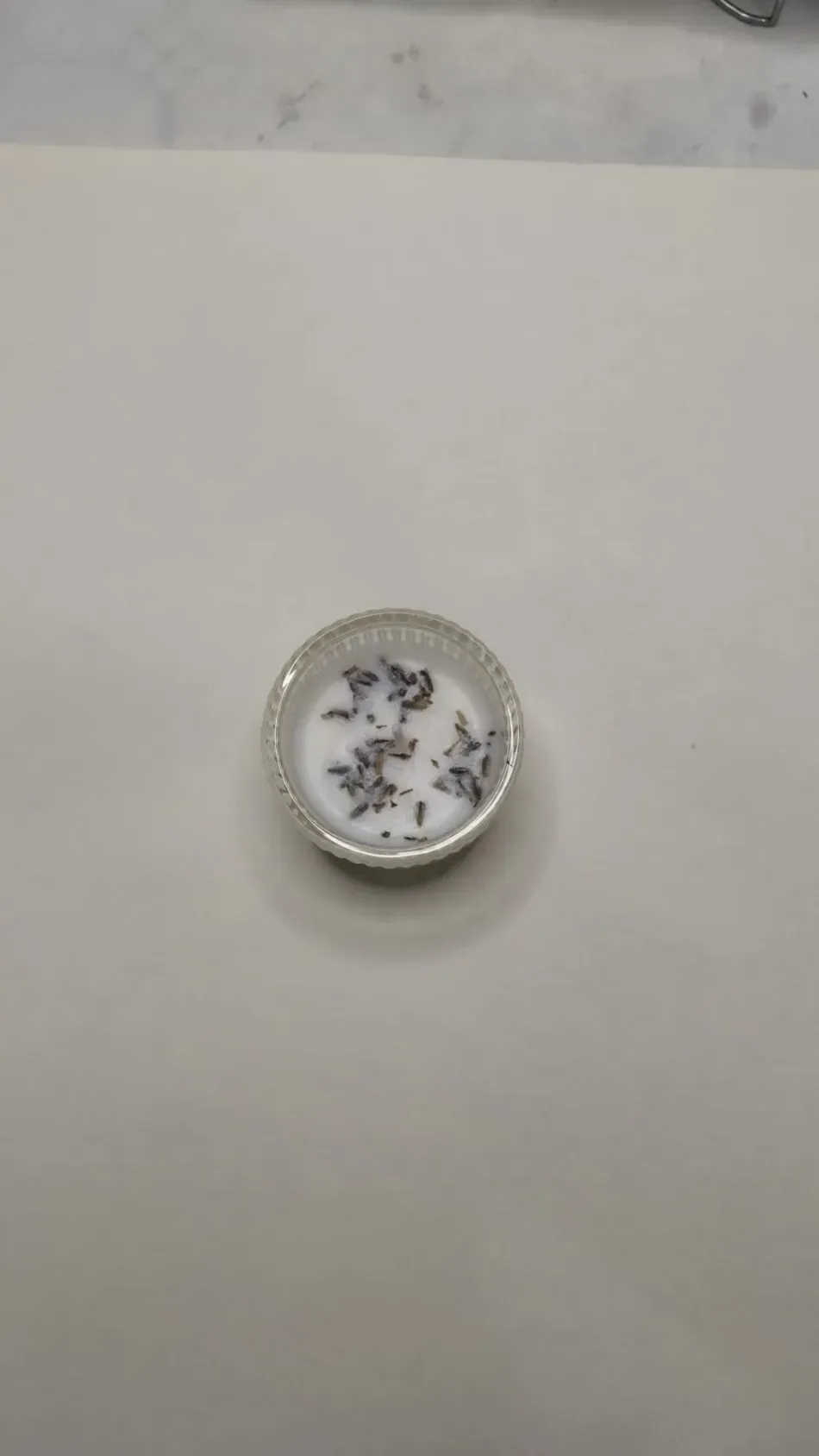 Pequeño objeto redondo de plata con una cara blanca y marcas oscuras en forma de estrella sobre una superficie lisa.
