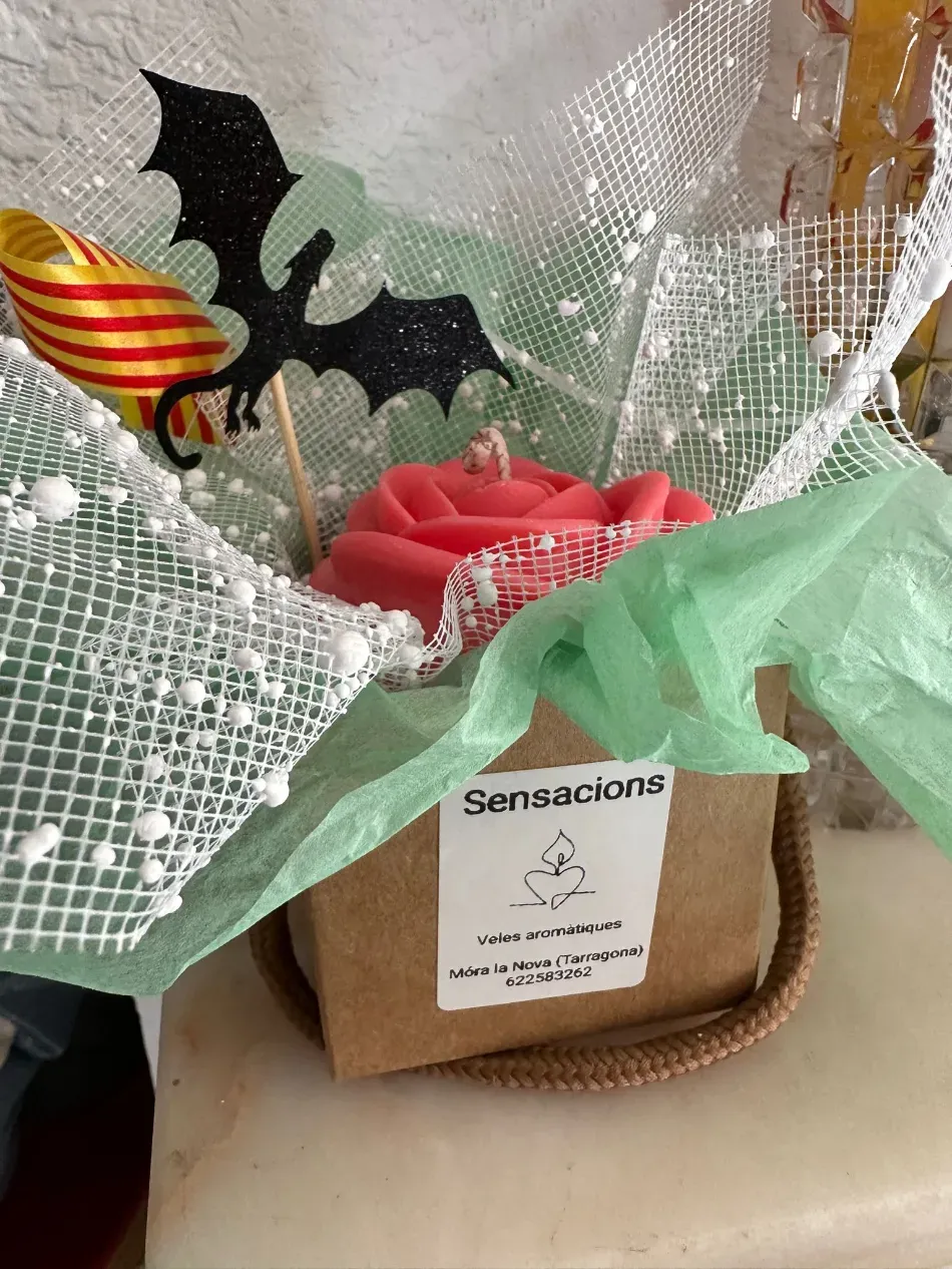 Cesta de regalo de Halloween con decoración de murciélago, flor roja y cinta verde envuelta en papel transparente.