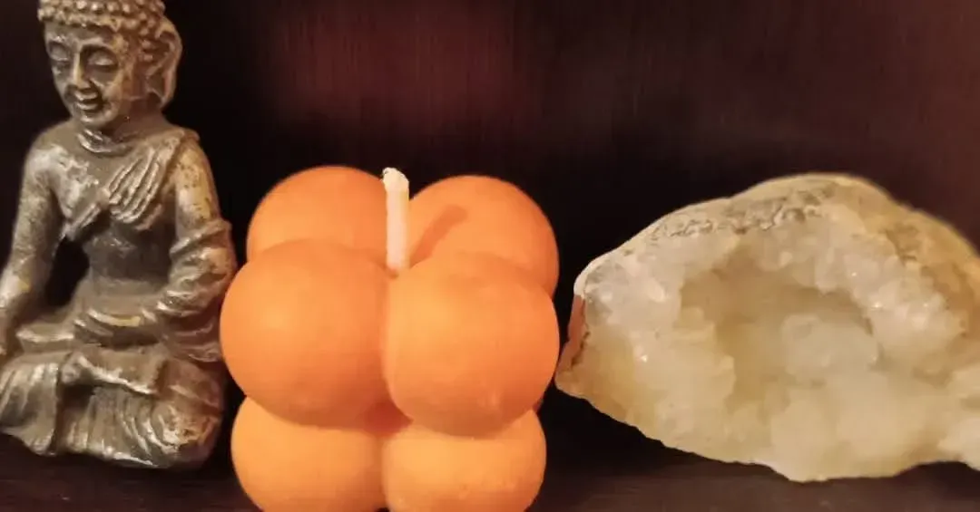 Estatua de Buda junto a una vela naranja y una piedra de cristal sobre una superficie oscura.