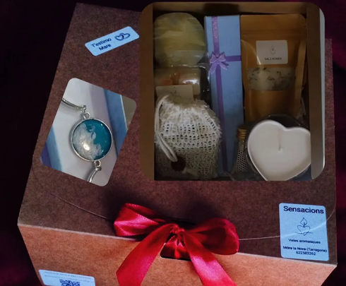 Caja de regalo con vela, collar con colgante y pequeños dulces envueltos y atados con una cinta roja.