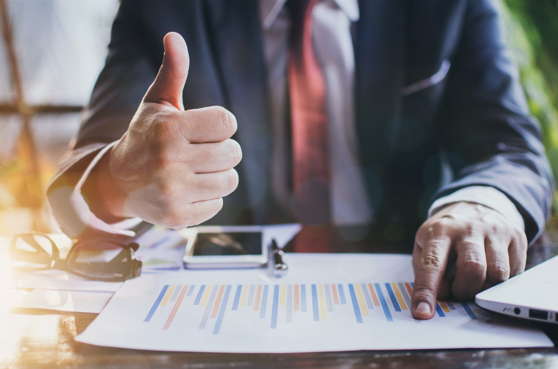 Persona de traje señala un gráfico financiero y hace un gesto de aprobación con el pulgar hacia arriba.