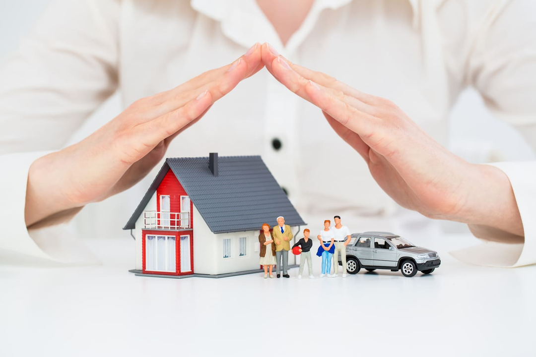 Manos ahuecando una casa en miniatura, figuras familiares y un automóvil, simbolizando protección.