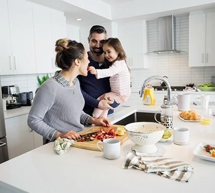 Familia de cuatro personas sonriéndose unos a otros, sentados en el suelo frente a un sofá, en el interior.