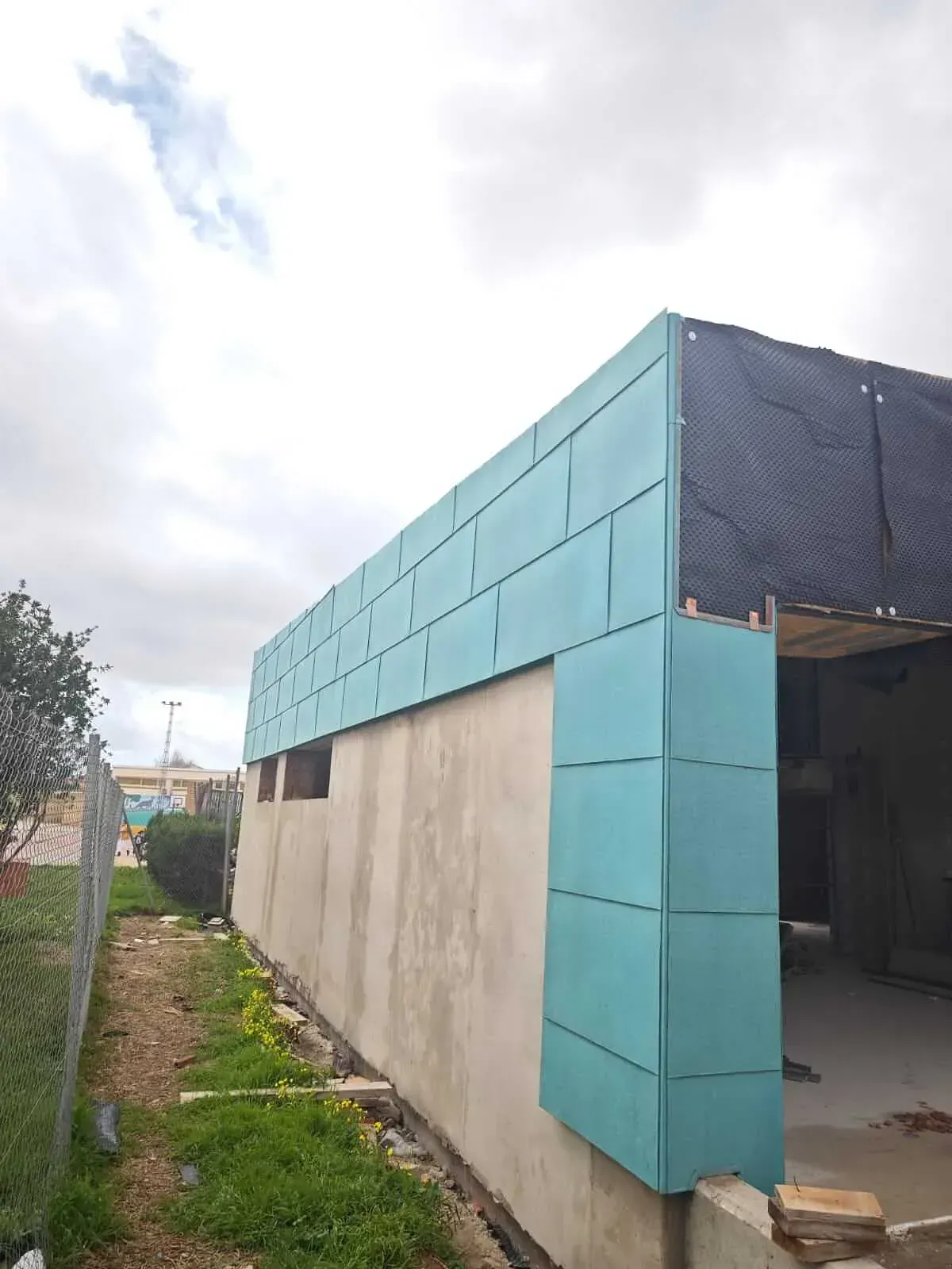 Al lado de una valla se está construyendo un edificio con tejado azul.