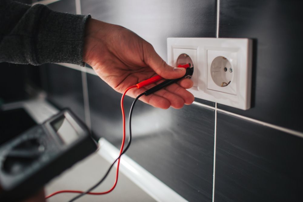 Una persona está midiendo el voltaje de una toma eléctrica con un multímetro.
