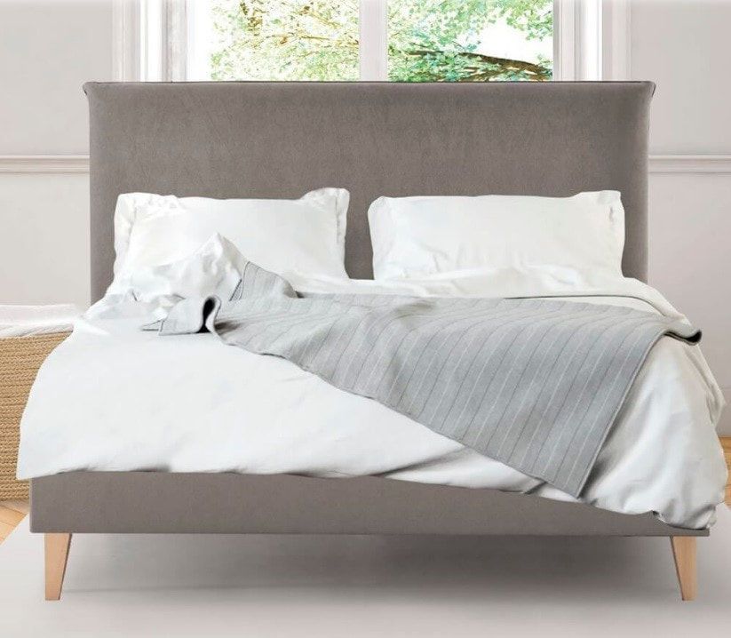 Una cama con sábanas y almohadas blancas y un cabecero gris.