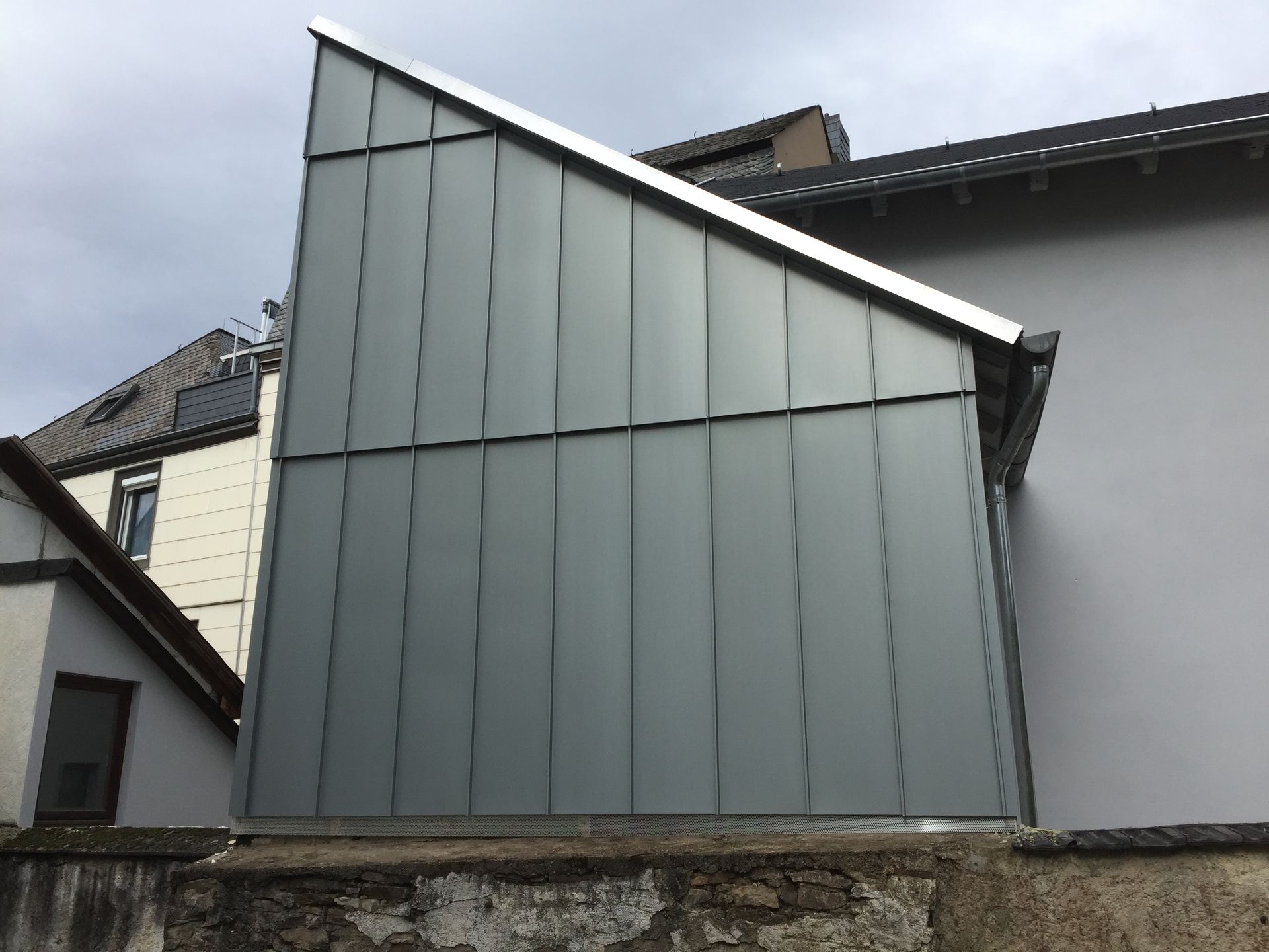 Grauer, metallverkleideter Anbau mit schrägem Dach und vertikalen Paneelen.