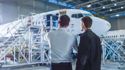 Deux personnes discutent, dans un hangar, d'un gros avion stationné sur une plateforme de maintenance métallique.