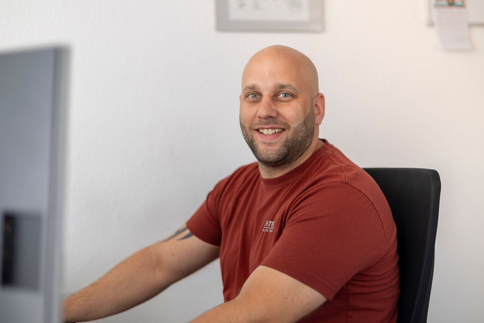 Ein kahlköpfiger Mann sitzt an einem Schreibtisch vor einem Computer.