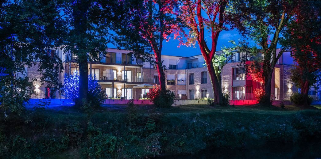 Ein großes Gebäude ist nachts beleuchtet und davor stehen Bäume.