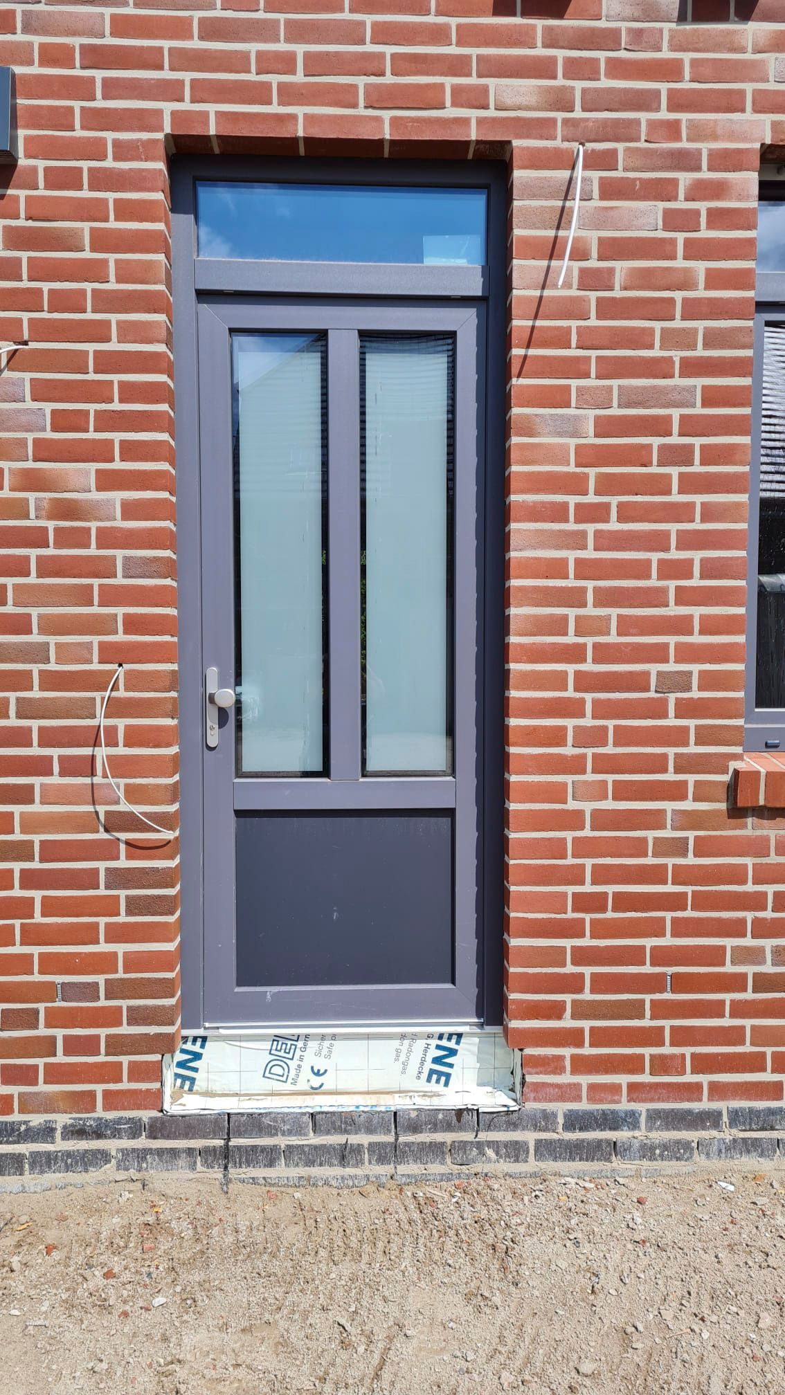 Ein Backsteingebäude mit einer grauen Tür und einem Fenster.